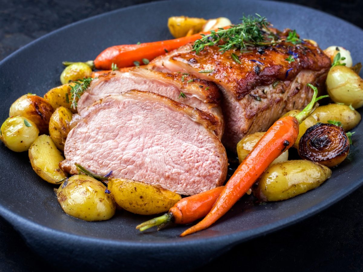Traditional roasted dry aged veal tenderloin with carrots and potatoes offered as closeup on a modern design cast iron plate